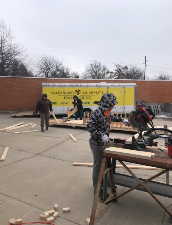 People work with wood outside near a Valparaiso University Engineering trailer on a cloudy day, participating in an American Society of Civil Engineers event.